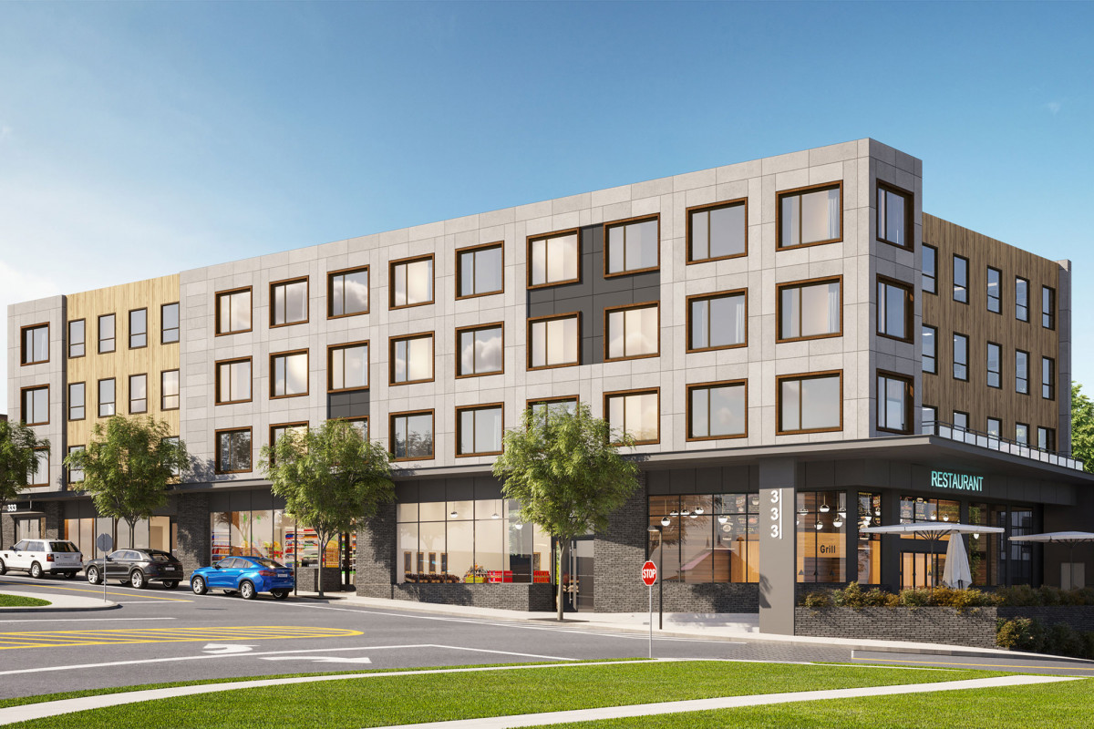 Grey apartment building with a ground floor and three upper floors. Blue sky in the background, green grass and an asphalt parking lot in the foreground.