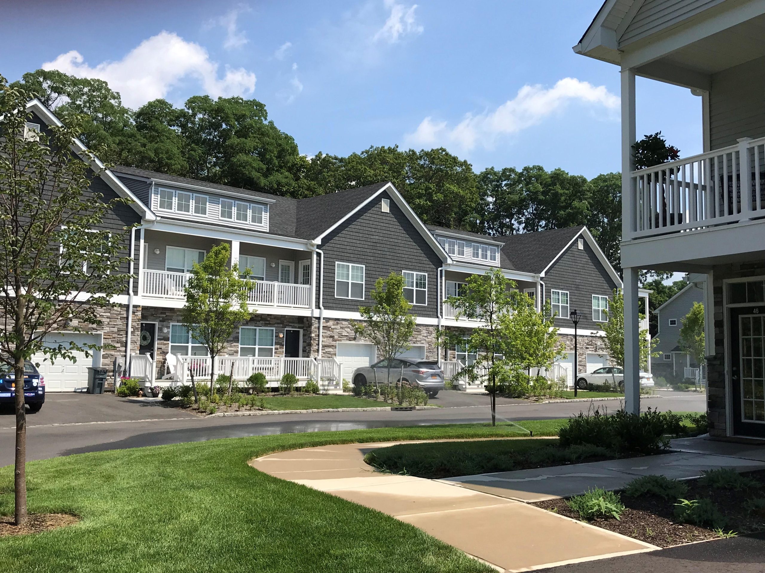 In the foreground, lush grass and a path lead to a complex of townhouses in the background. The complex is grey with white trim.