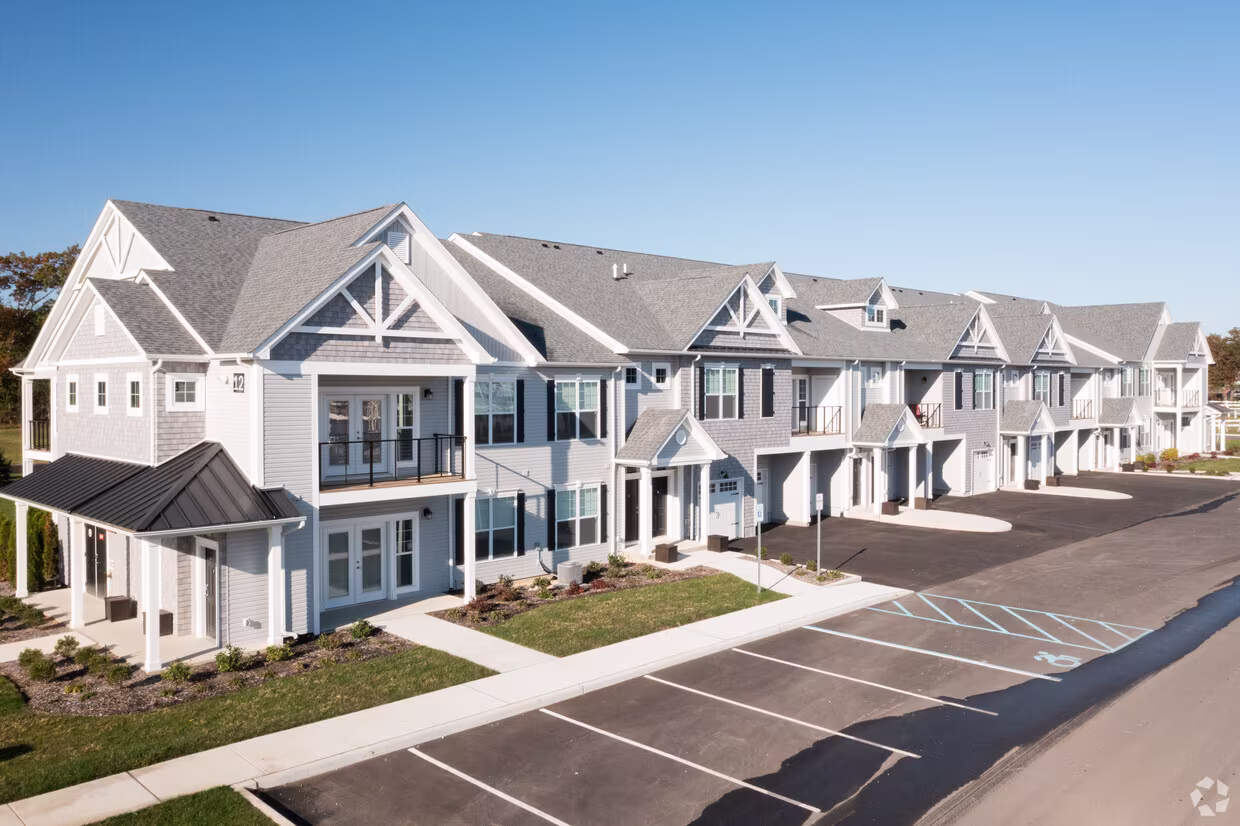 Grey and white building of rental units with lawns and parking spaces in front.