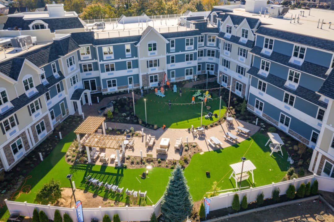 Aerial image of a large apartment complex with a lawn and gathering space in front.